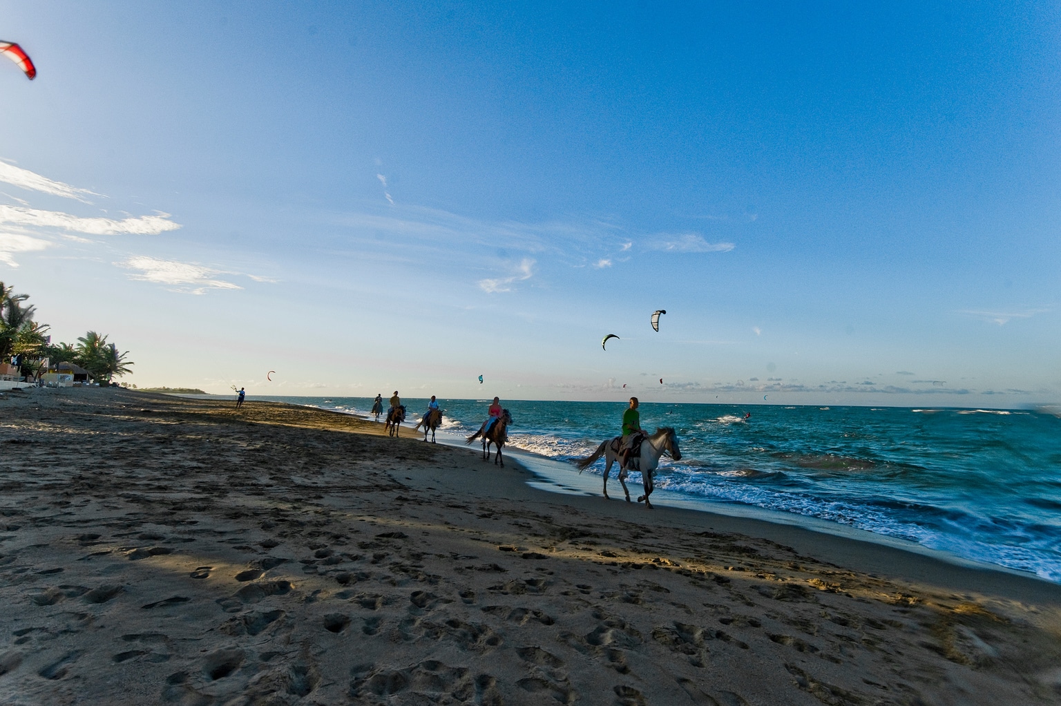 people-horseback-riding-on-beach-sand-turquoise-ocean-sunset