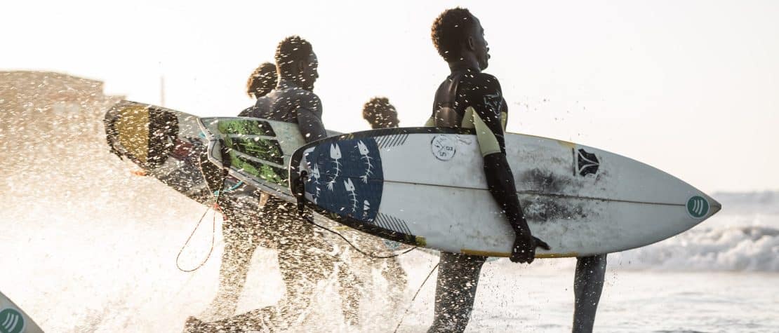 surfers in senegal running in water with surfboards at Copacabana Surf Village