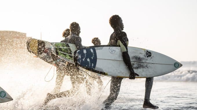 surfers in senegal running in water with surfboards at Copacabana Surf Village