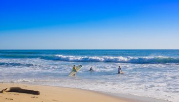 Outdoor view of surfers on the beach of Santa Teresa in a beautiful sunny day with blue sky and blue water in Costa Rica.