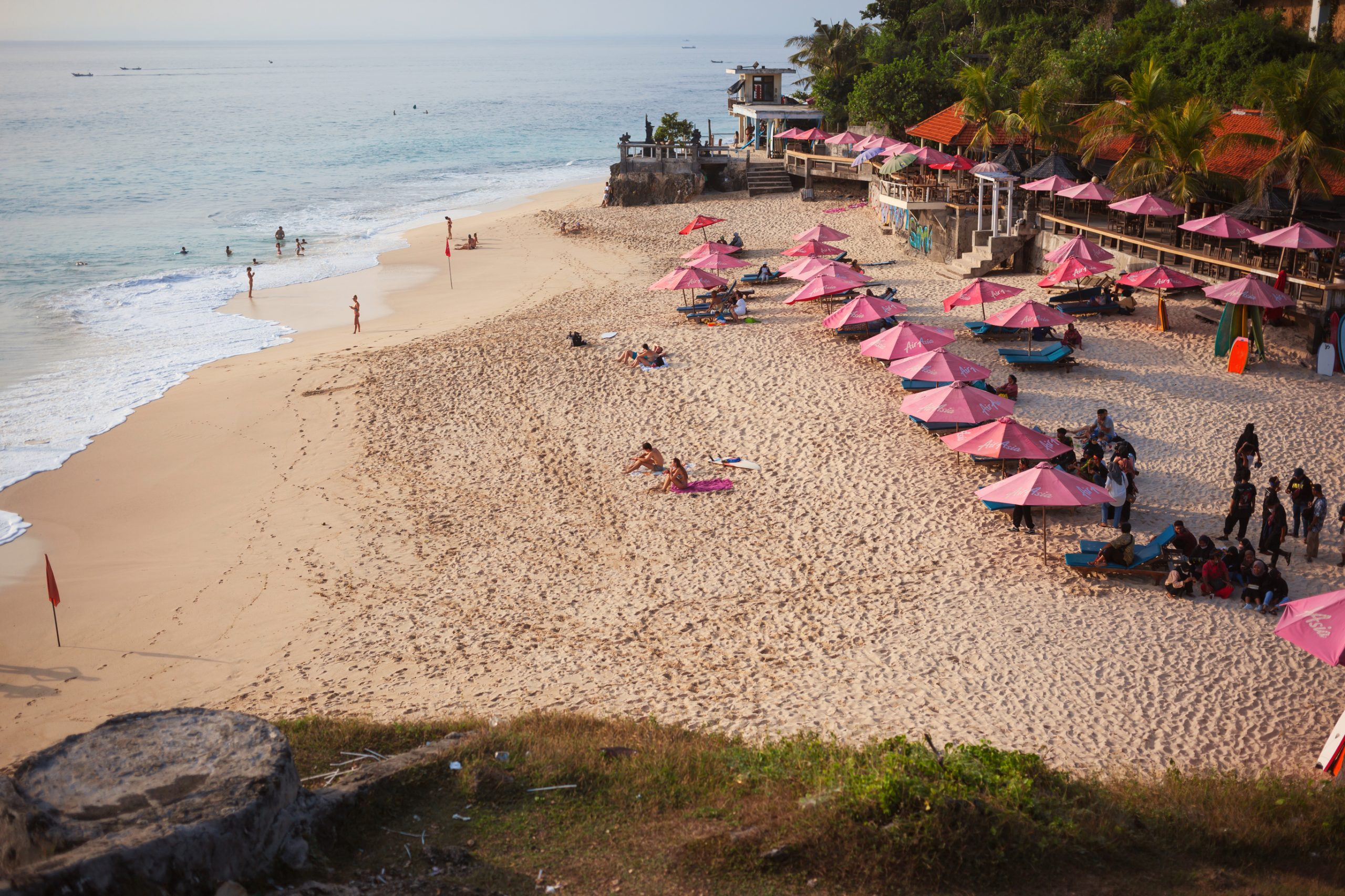 Dreamland beach with pink umbrellas and sunnbeds on white sand at sunset.